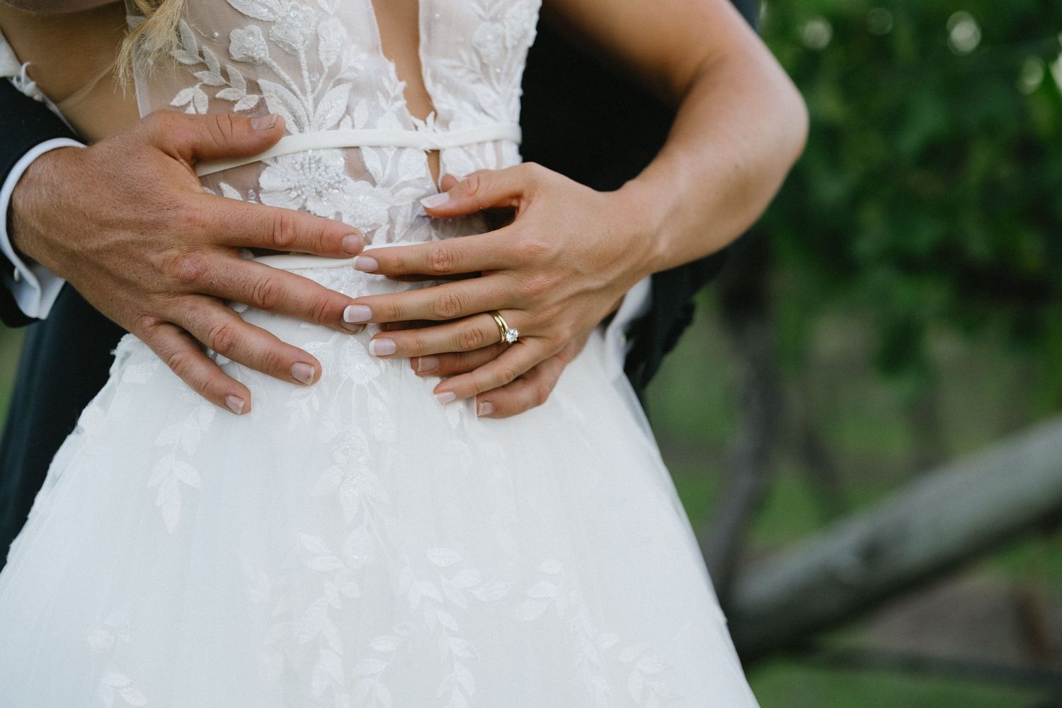 Close up of couple's hands embracing around bride's waist showing wedding rings.