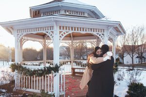 A couple dances together in romantic moment under a white gazebo decorated with holiday greenery at sunset.