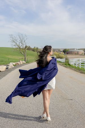 A figure in a white dress twirls on a country road, with a flowing navy blue shawl billowing in the wind.