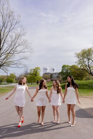 A group in matching white dresses walking together on a path with city buildings visible in the distance.