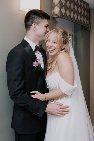 Newly married couple shares intimate laughing moment together in formal wedding attire.