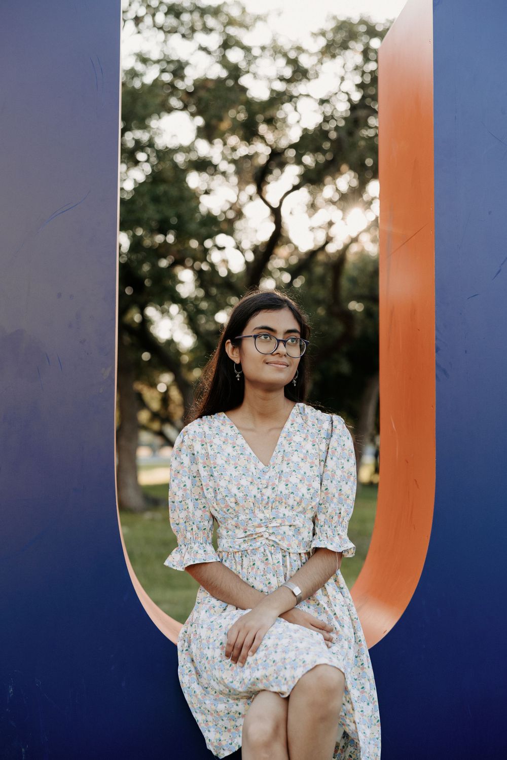 San Antonio Graduation. A portrait of someone sitting on an orange and blue curved structure outdoors.