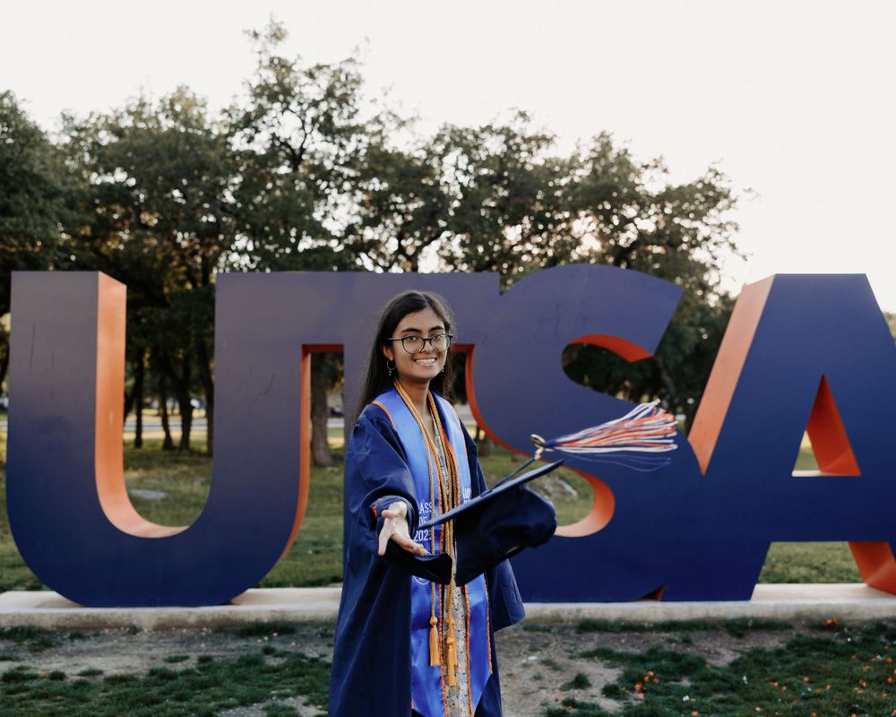 San Antonio Graduation. A graduate poses in front of large UTSA letters wearing graduation regalia.