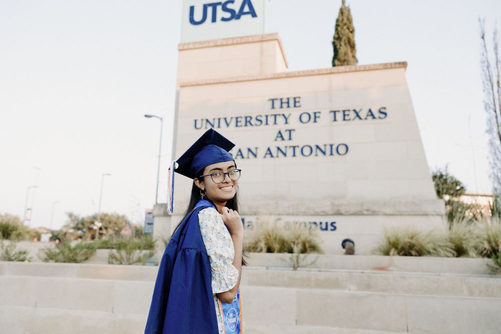 San Antonio Graduation. A graduate stands in front of the University of Texas at San Antonio campus sign.