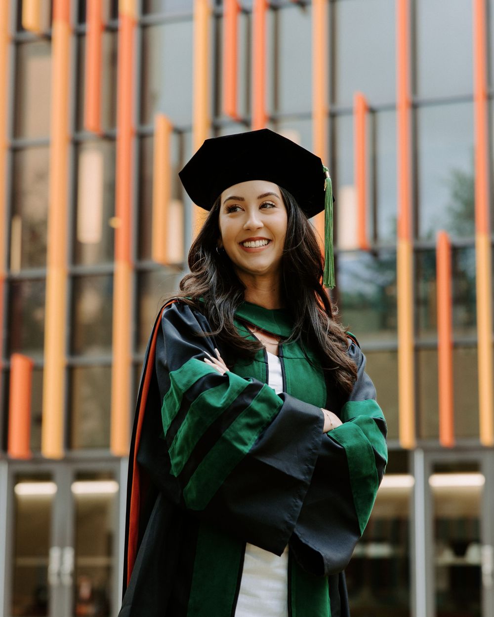 San Antonio Graduation. Graduate wearing traditional green academic regalia with doctoral hood and cap stands smiling outside UT Health SA.