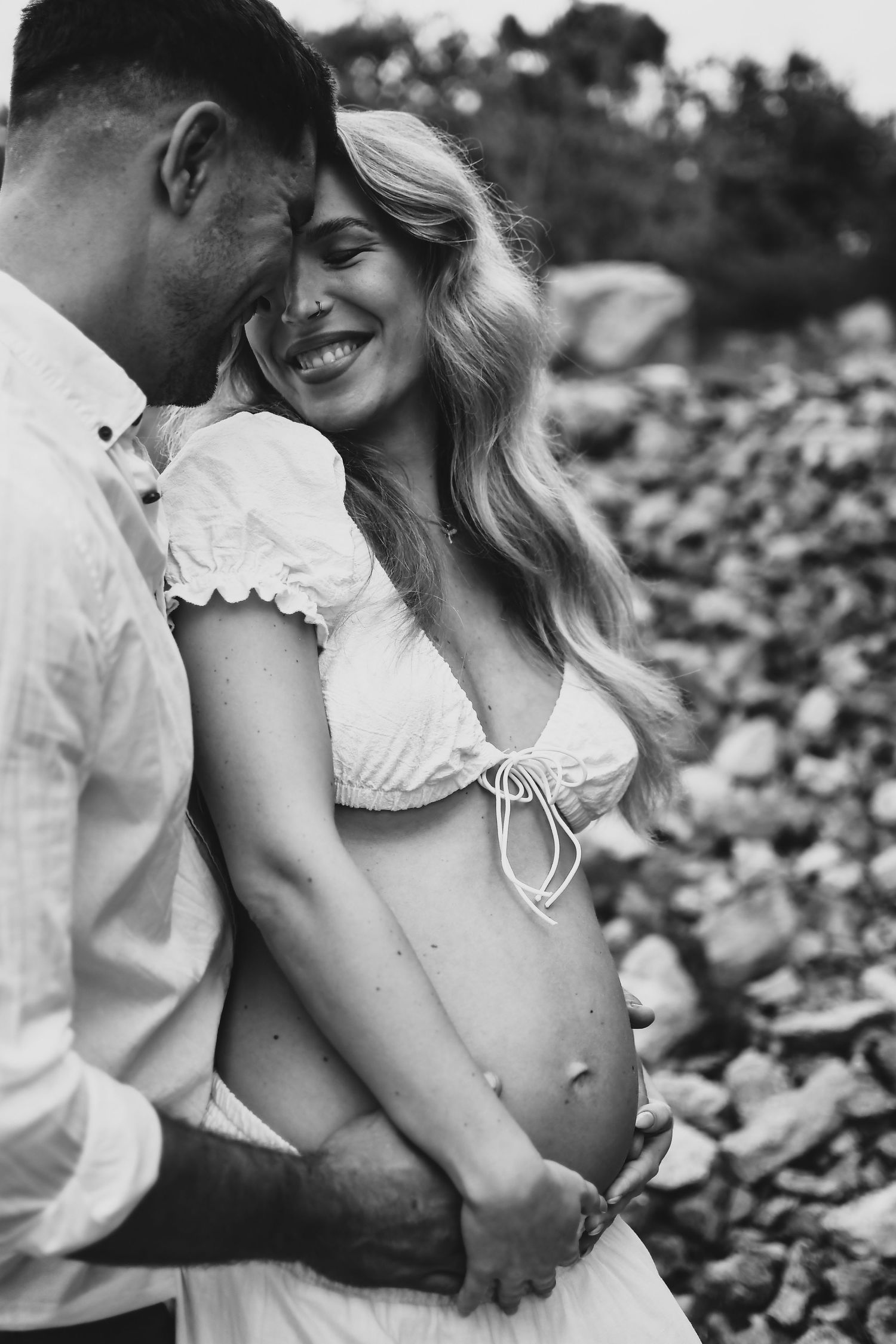 Black and white maternity photo of couple embracing on rocky terrain.