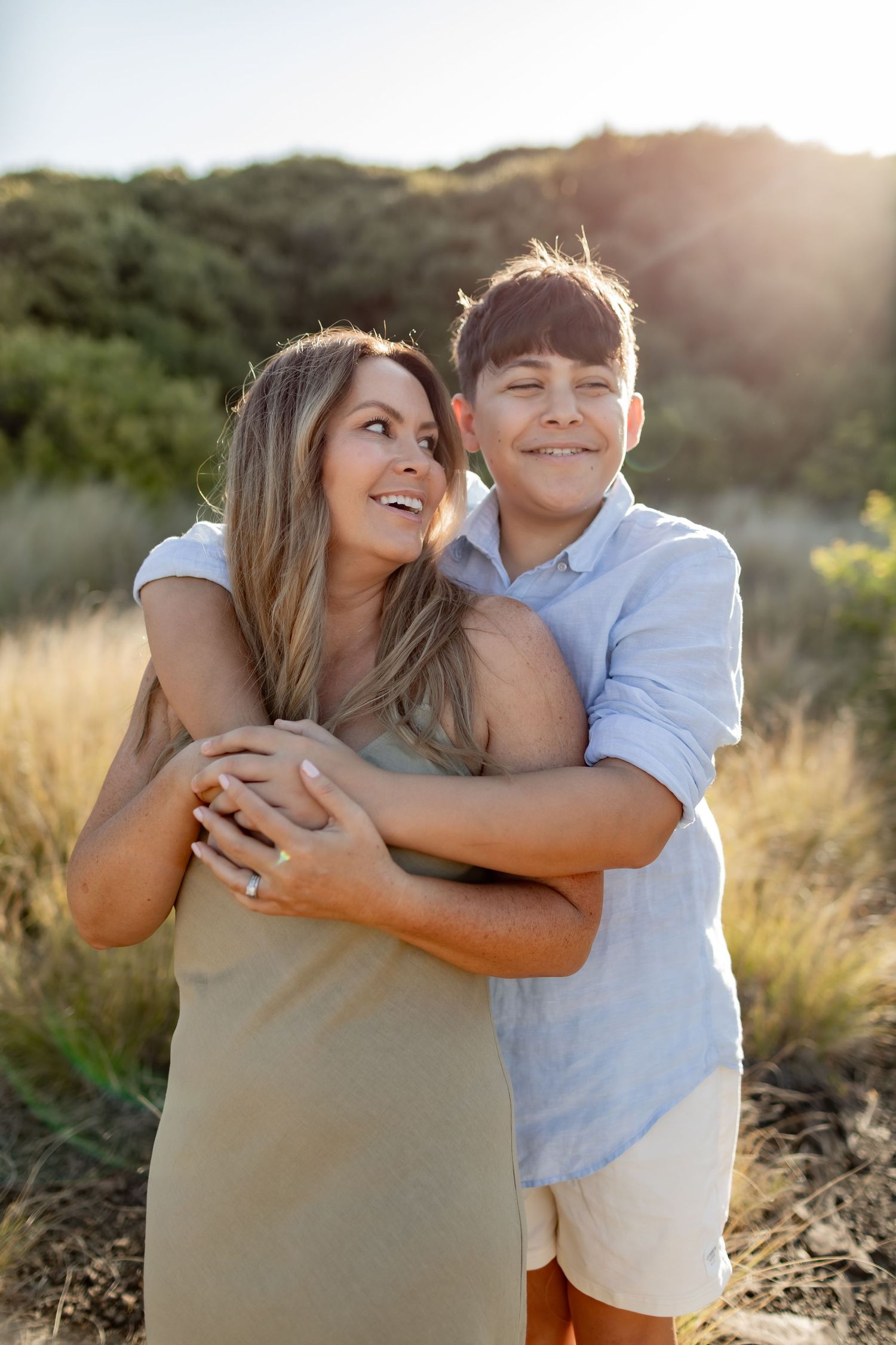 Two figures embracing and laughing together on a sunlit hiking trail.