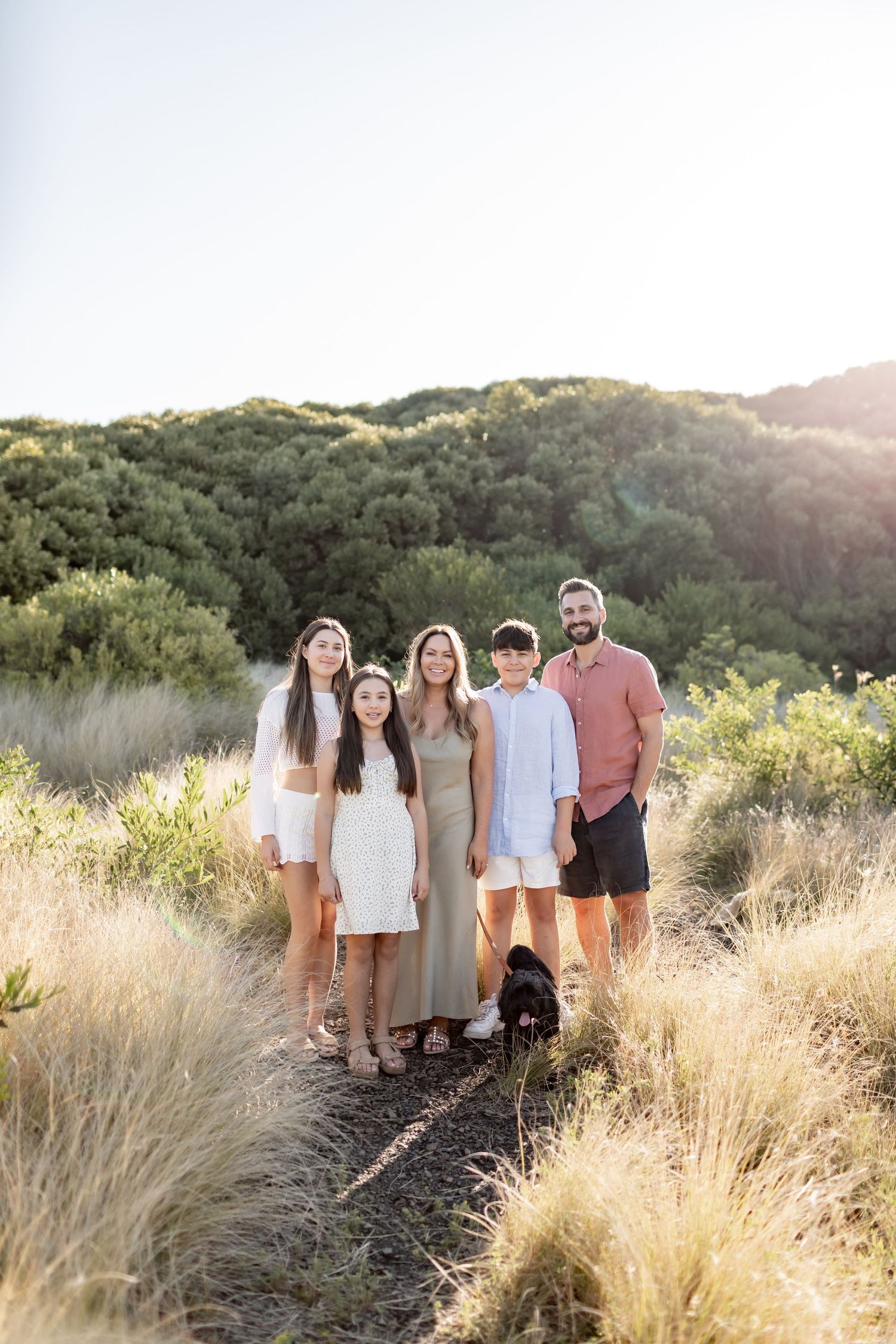 A group poses together on a nature trail with their black dog during golden hour sunset.