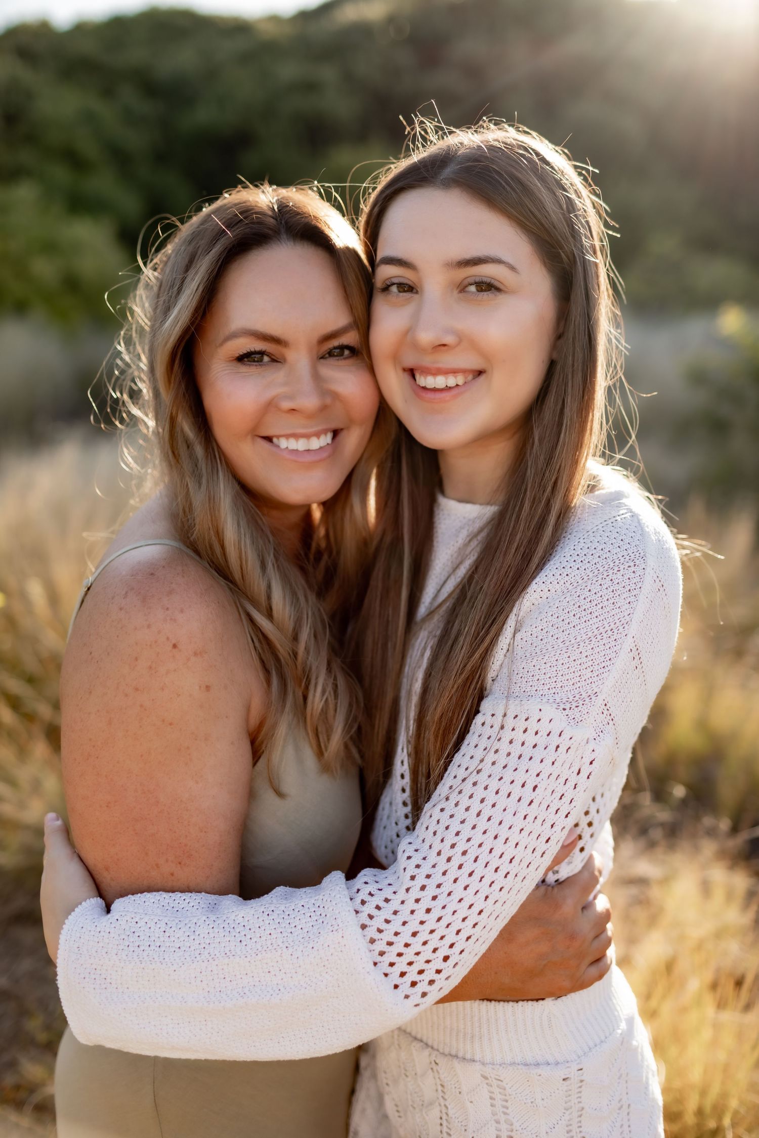 Two people in white and beige clothing embracing and smiling during a golden hour photoshoot.