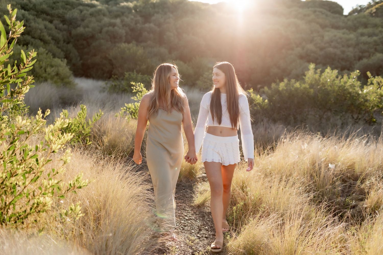 Two people walking together on a natural trail during sunset with golden grass surrounding them.