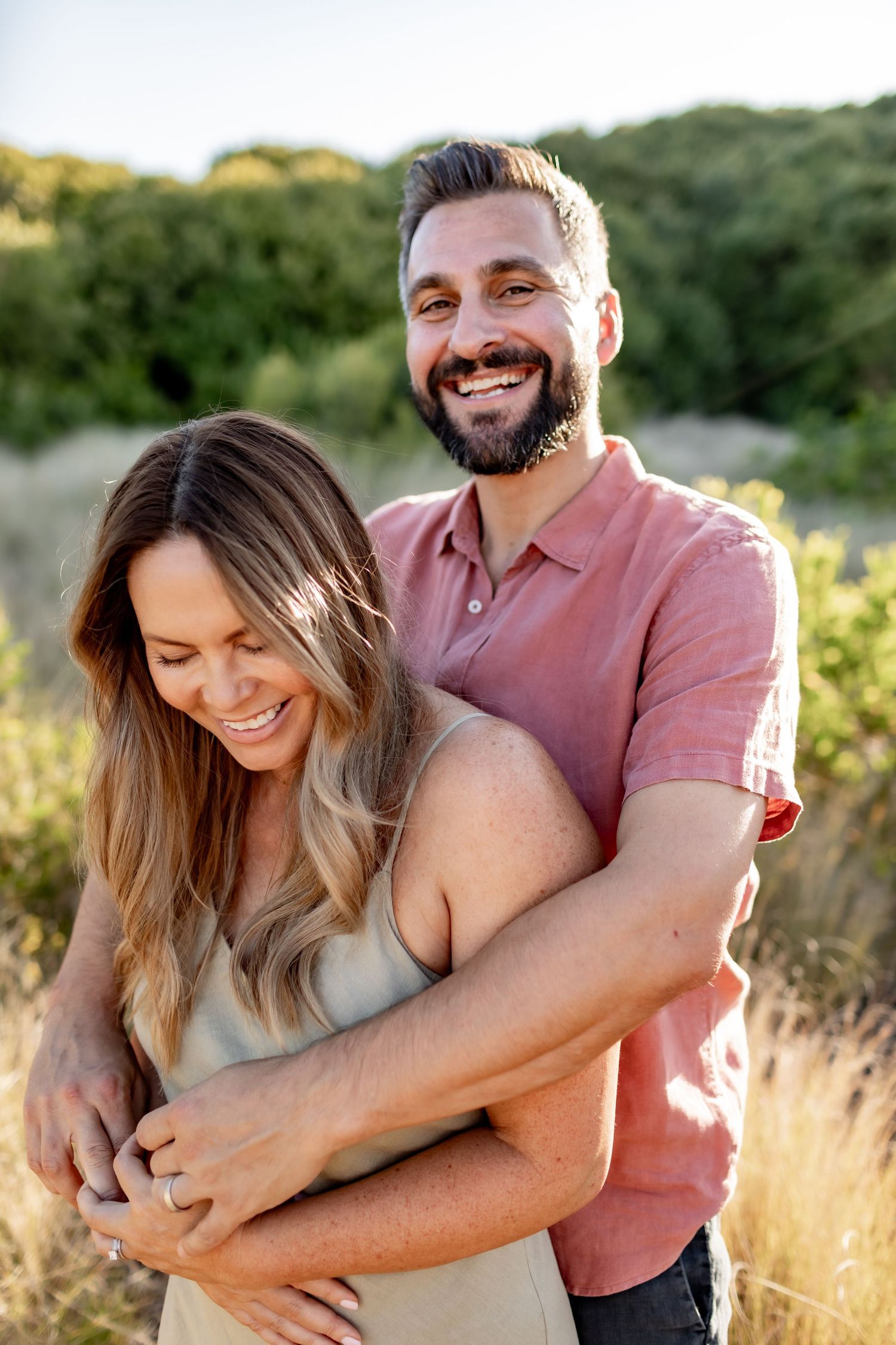 Couple sharing candid laughing moments together in a golden field during sunset photo session.