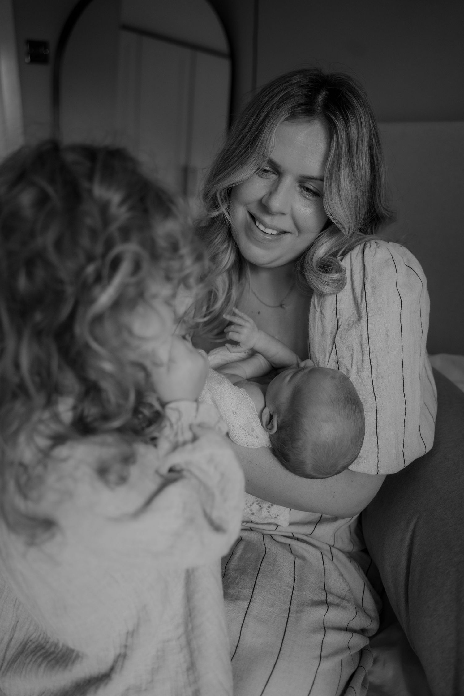 Parents cuddling their baby in soft morning light during an at-home newborn photoshoot in Leicestershire.