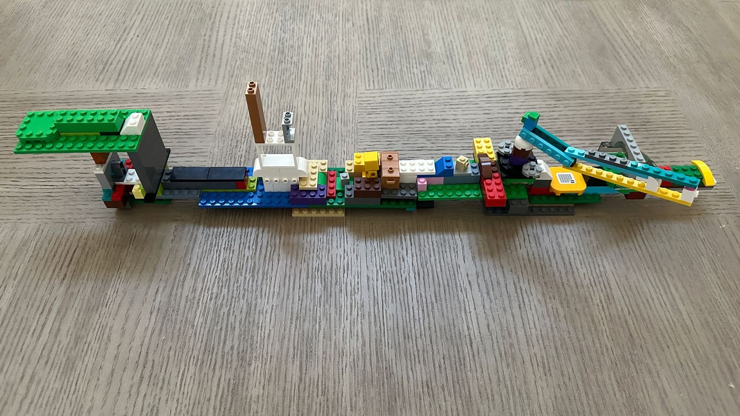 Colorful LEGO bricks assembled into a long chain design with various pieces connected across a wooden surface.
