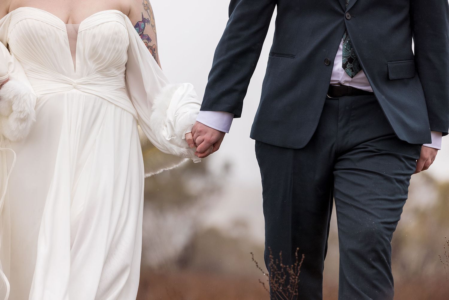 Close-up view of a bride in a white gown holding hands with groom in dark suit at an outdoor ceremony.