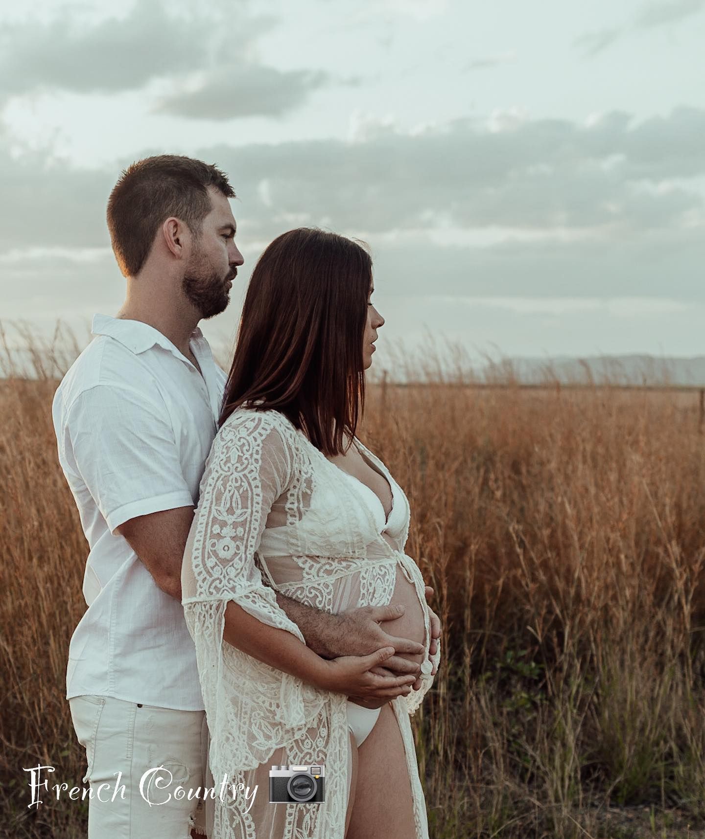 A romantic couple embraces in a serene wheatfield at sunset as the tall grass sways around them.