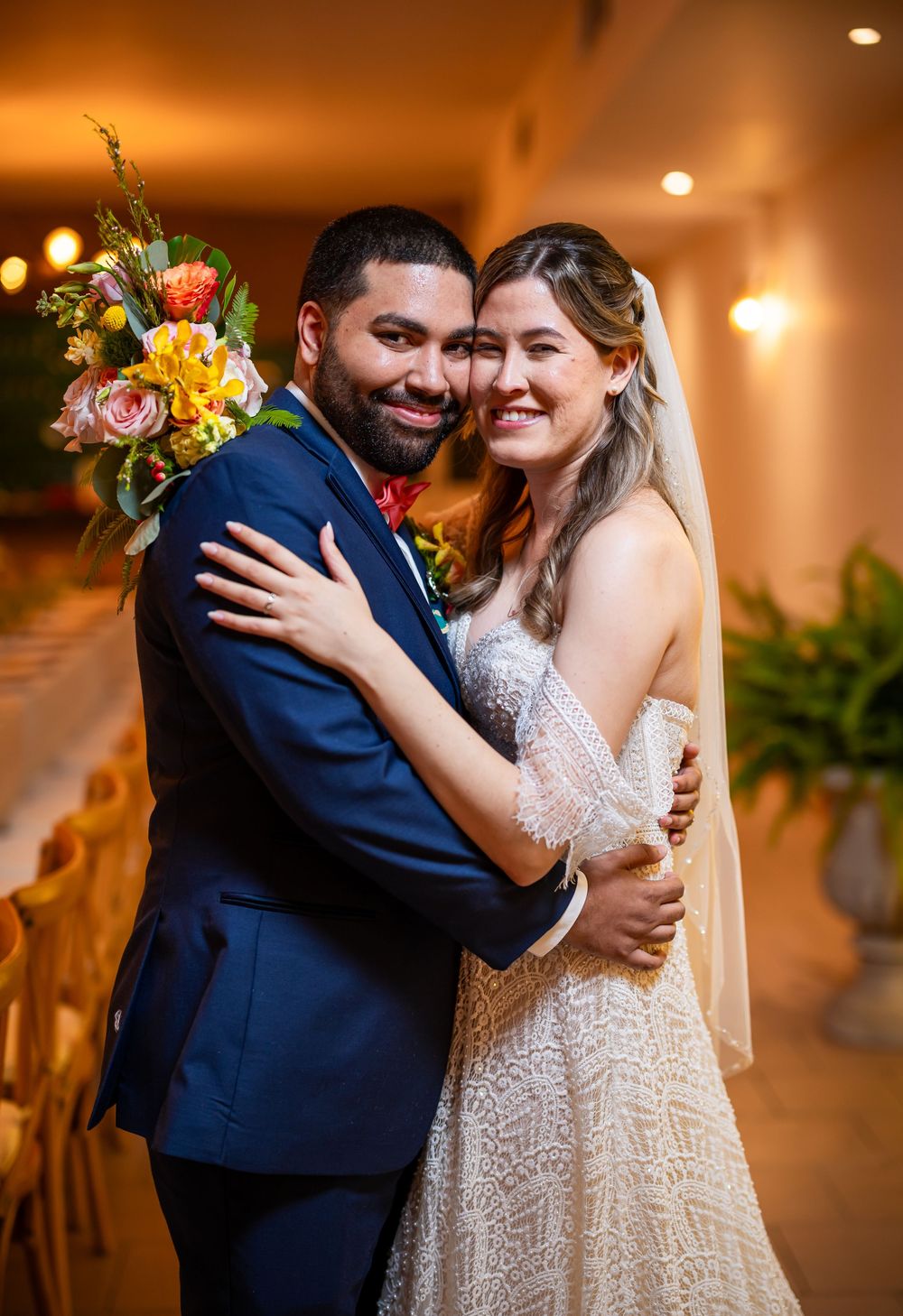 Couple in embrace shares tender moments during indoor wedding reception with warm lighting.
