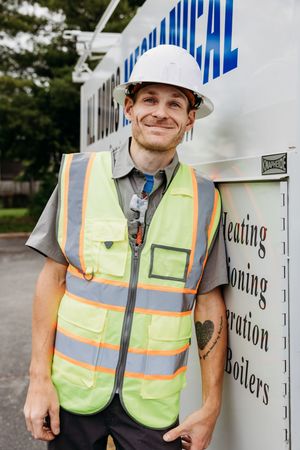 Construction worker wearing yellow safety vest and hard hat stands next to white equipment container outdoors.
