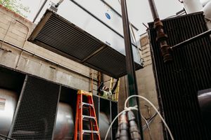 Construction workers on ladders installing black metal ceiling panels in an industrial space.