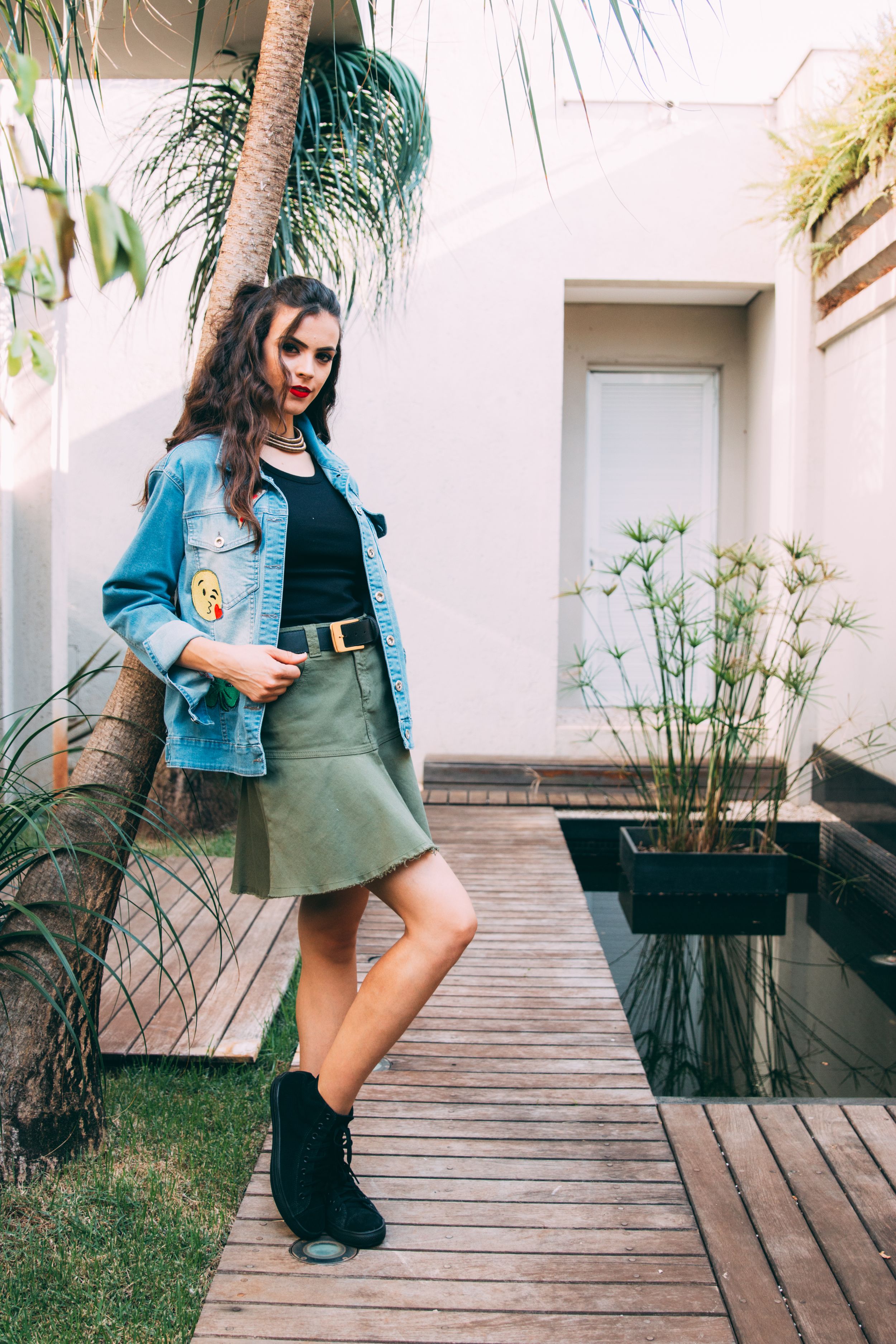 Person wearing a denim jacket and green skirt shown across four fashion poses on a wooden walkway with plants nearby.