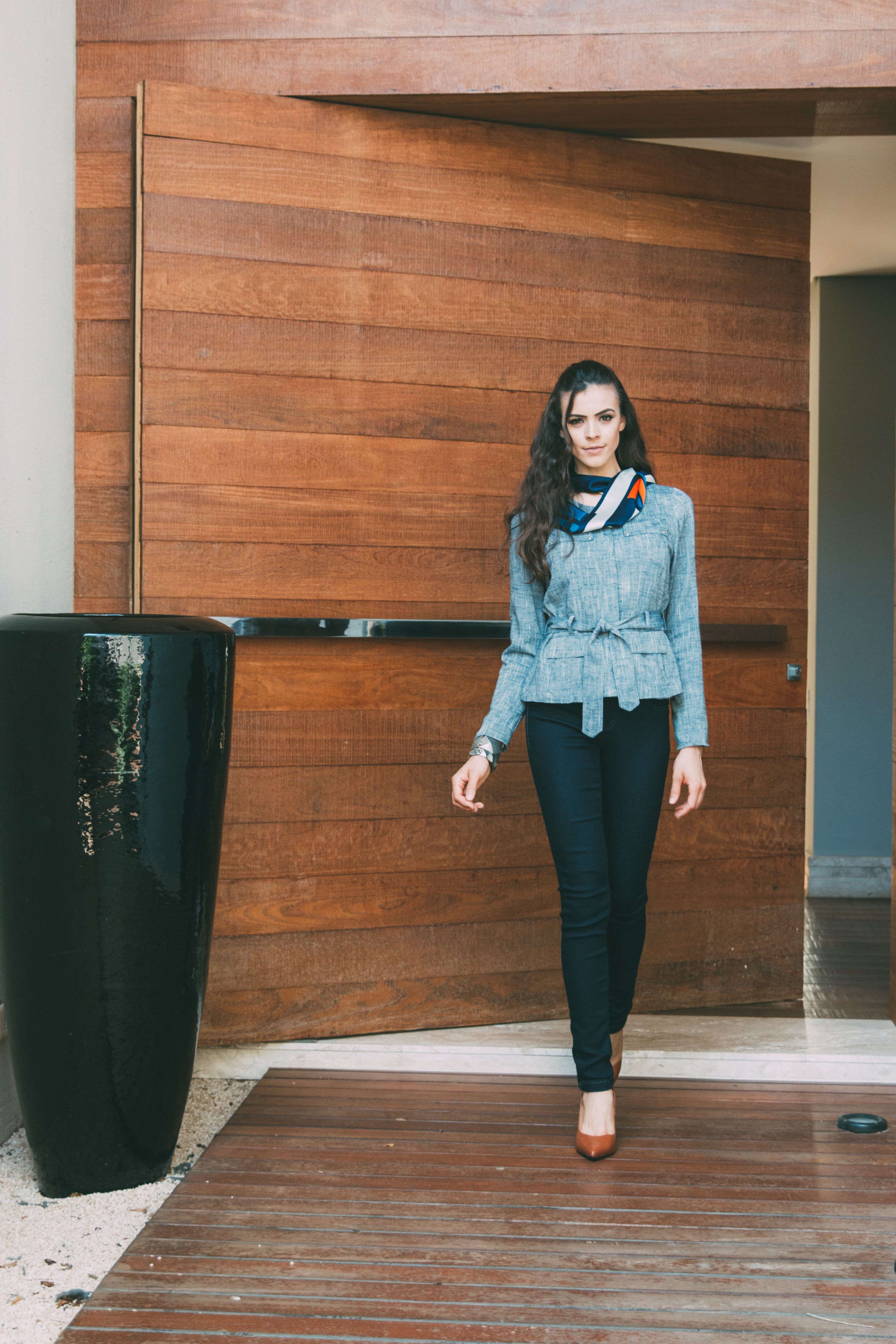 Woman poses in stylish tweed jacket and dark skinny jeans against wooden wall backdrop with modern decor.