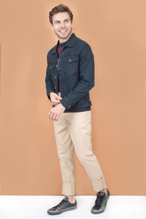 Person in denim jacket and khaki pants demonstrates casual outfit with dark sneakers against beige background.