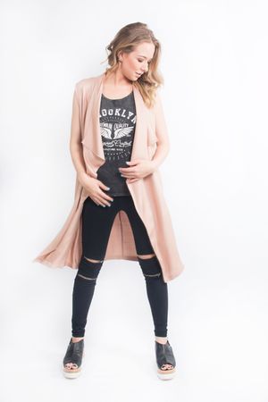 Model wears a blush pink long cardigan over Brooklyn graphic tee with distressed black jeans and platform sandals.