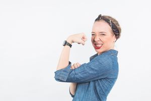 Excited person in denim top showing bicep flex pose against white background with big smile.