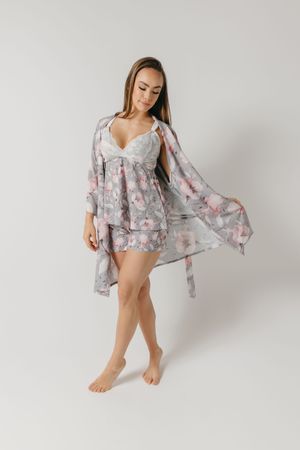 Fashion model wearing flowy floral print robe in pink and gray against white background.
