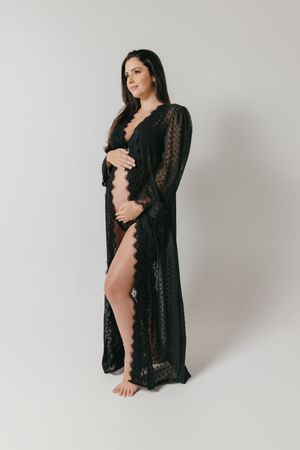 An elegant black lace maternity robe with sheer sleeves shown in a minimalist studio photoshoot.