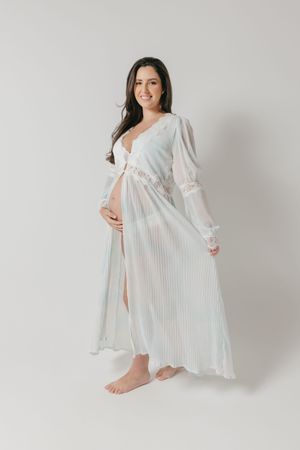 Ethereal white maternity gown with long sleeves and lace details shown on a light grey studio background.