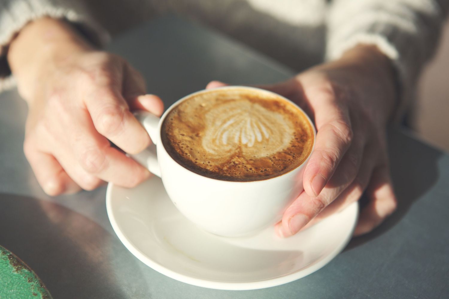 Multiple closeup shots of hands holding white coffee cups with latte art designs.