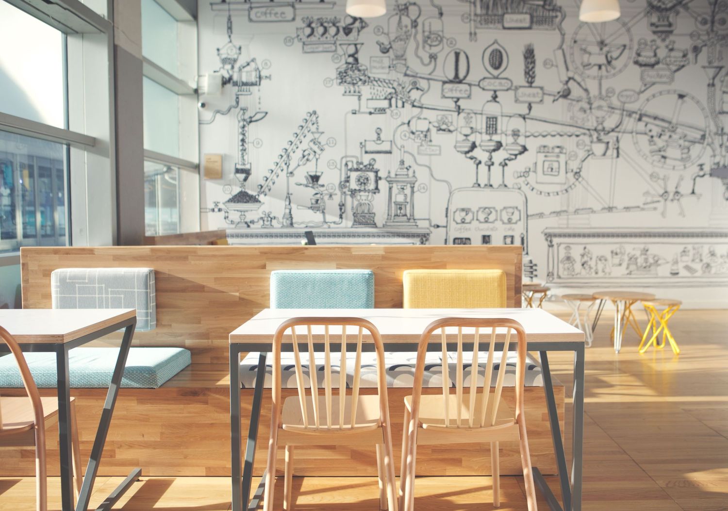 Modern cafe interior with white chairs, wooden tables, and creative sketched doodle artwork covering the wall.