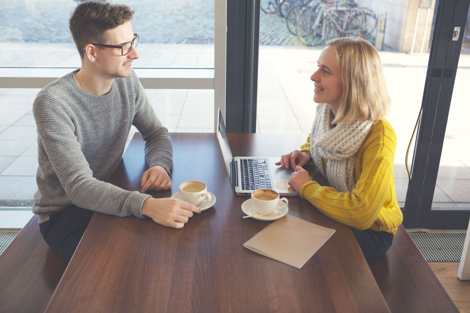 Group of people having coffee and conversation at bright modern cafe table by window.