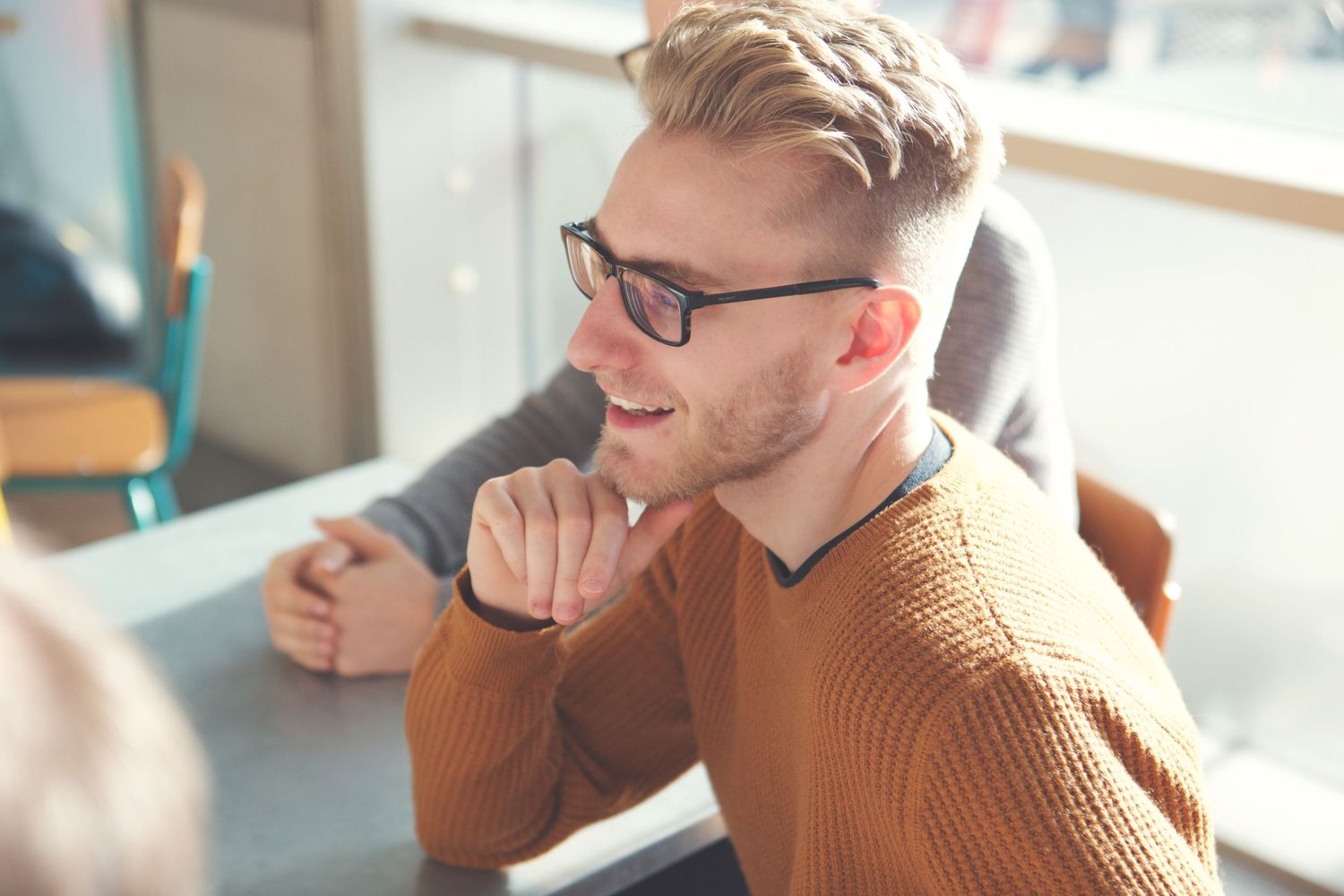 Two colleagues smile during discussion while sitting at desk in bright office setting.