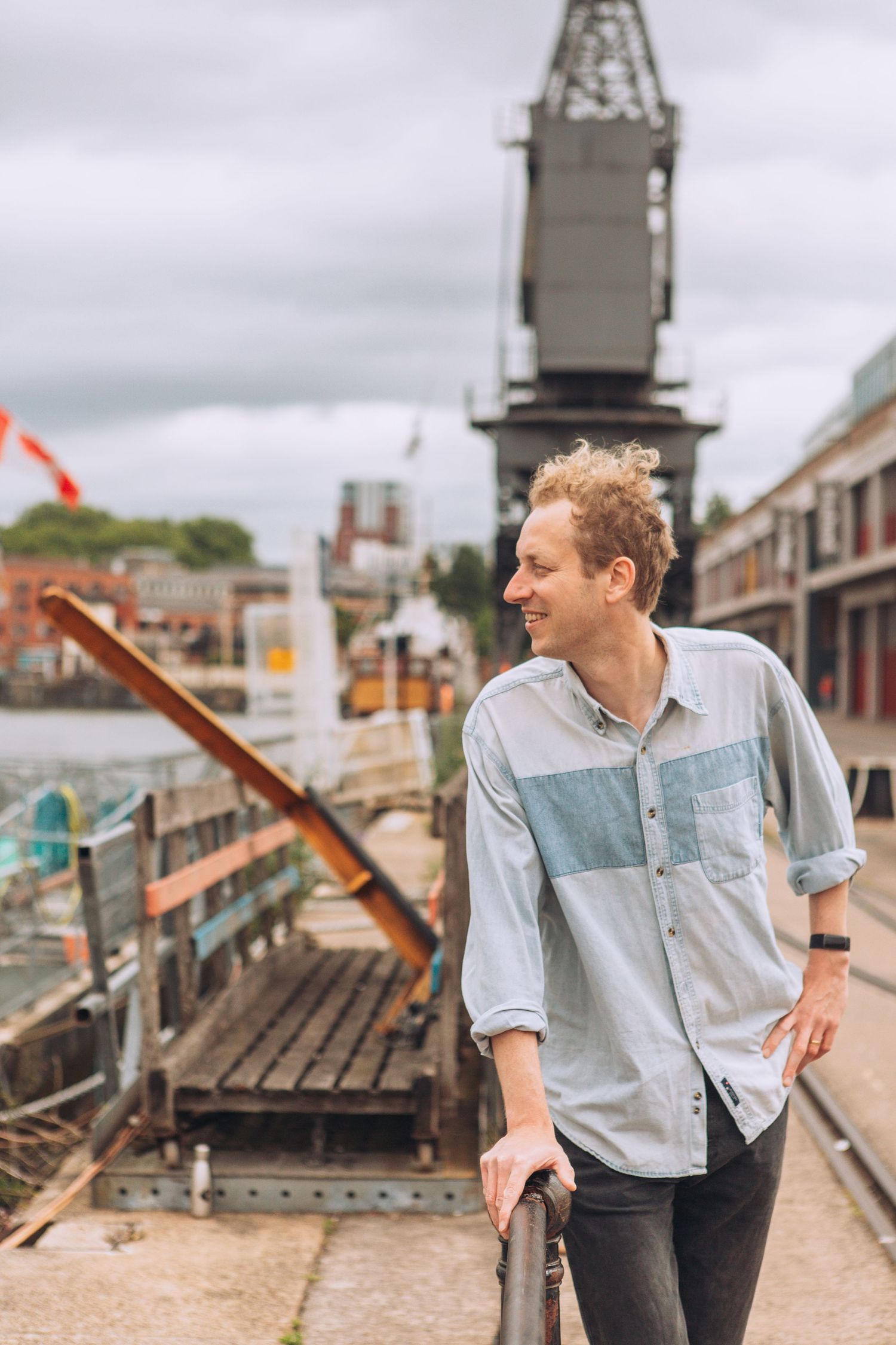 Someone in a casual denim shirt smiles while standing on an industrial rooftop with city buildings in the background.