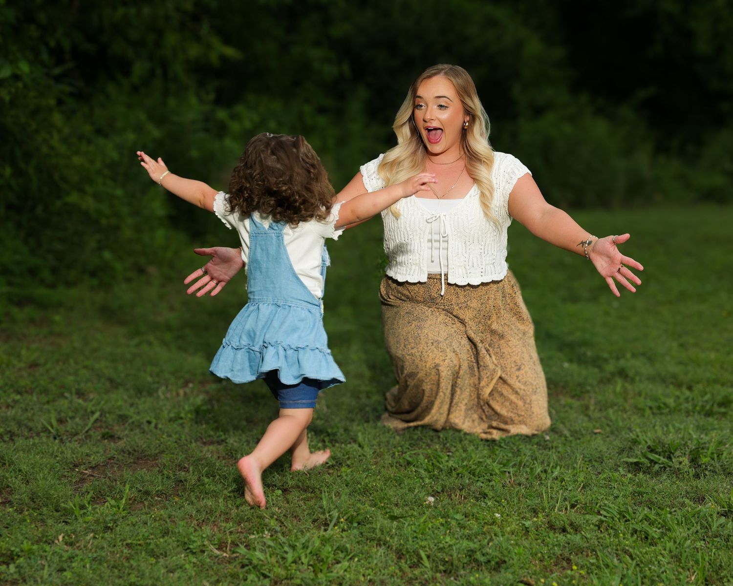 Two people share a joyful moment dancing and jumping together on green grass during a sunny outdoor photo session.