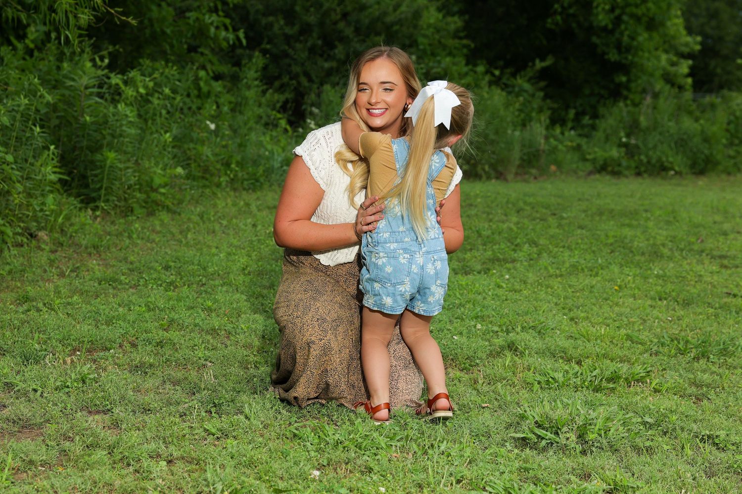 A person and small child share a joyful moment together while kneeling in a green grassy field.