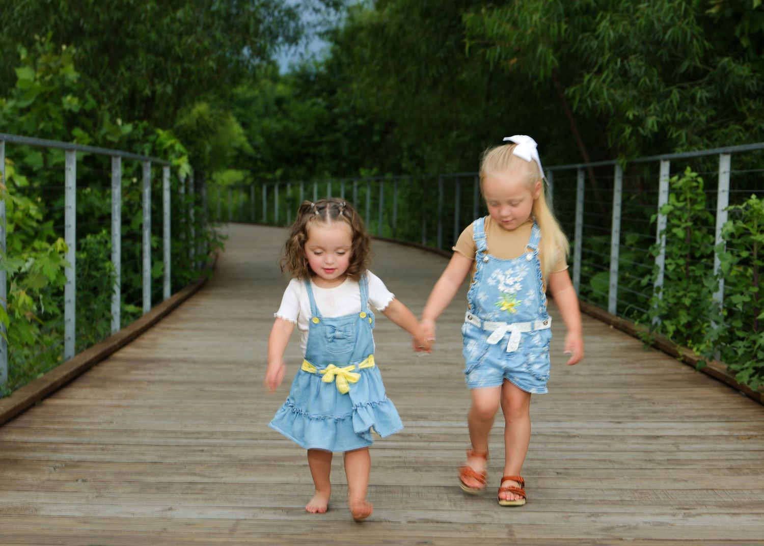 Two small children walk hand in hand along a wooden boardwalk path through lush green scenery at Osage park in Bentonville Arkansas