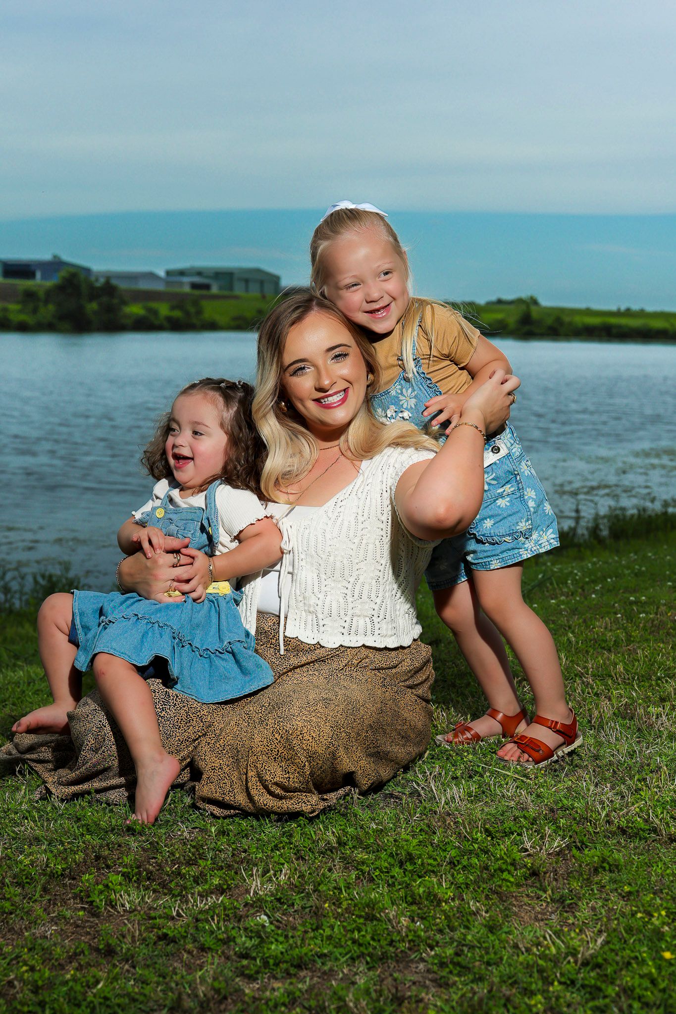 Two people sitting on grassy ground by a lake on a sunny summer day, sharing joyful moments together.