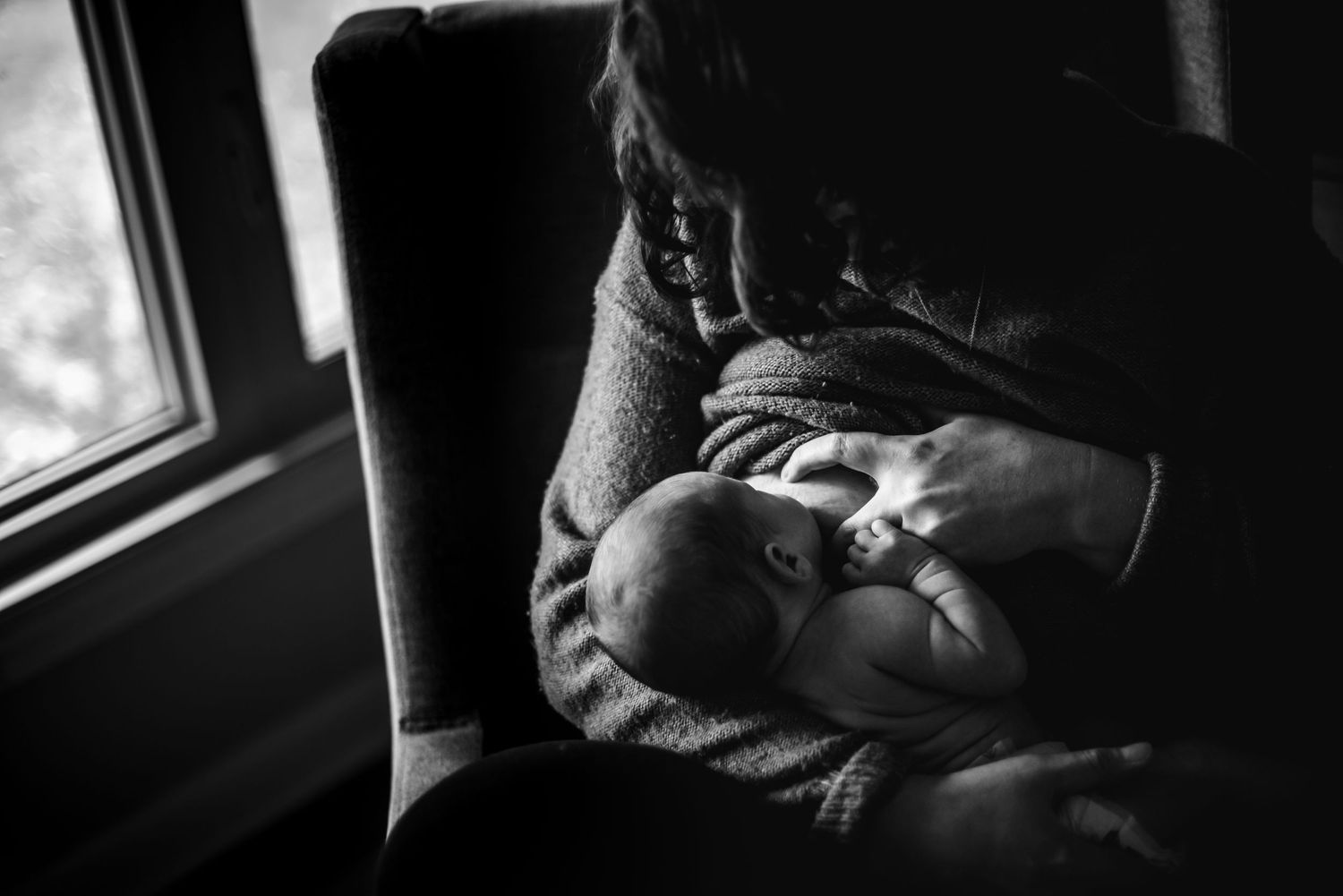 A tender black and white intimate moment between parent and baby by a window in soft natural light.