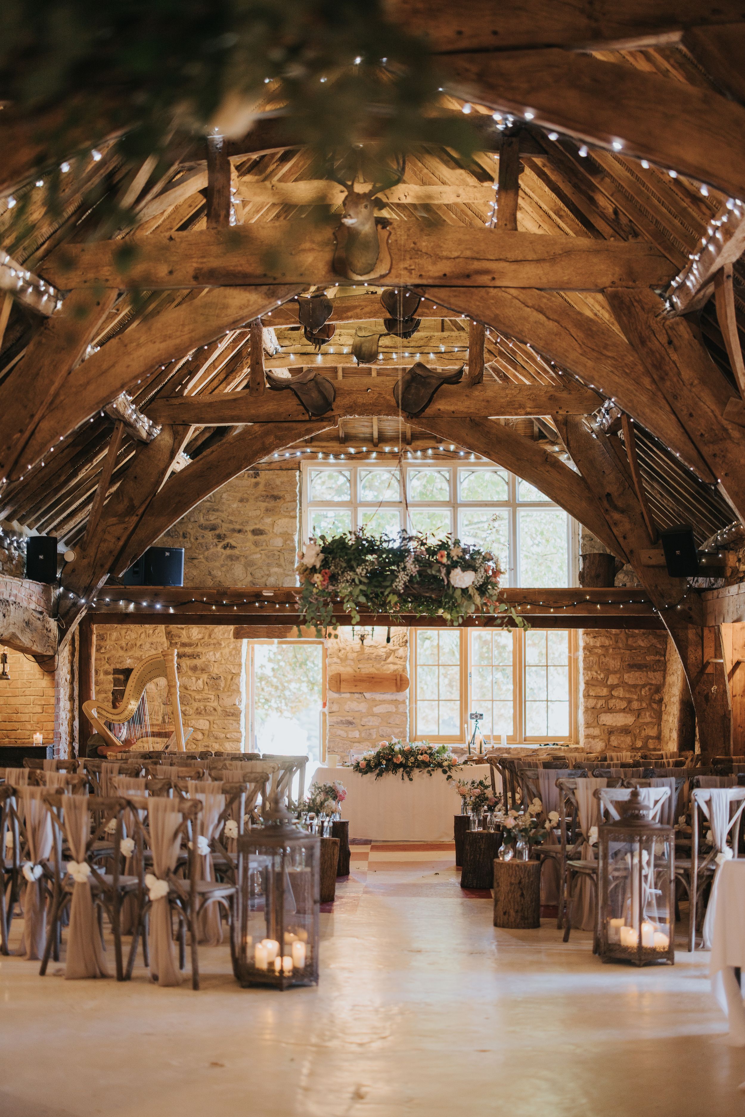 Rustic barn venue decorated with string lights and lanterns for an elegant wedding ceremony with vaulted wooden beams.