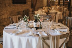 Elegant round table setting with crisp white linen, wine glasses, and delicate floral centerpieces in a rustic venue.