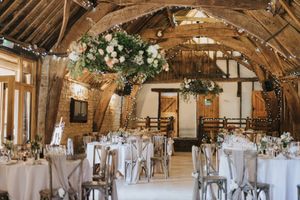 Rustic barn wedding reception venue with white floral arrangements and round tables set for dinner under exposed beams.