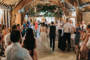 A lively reception celebration inside a rustic barn venue with timber beams and natural light streaming through windows.