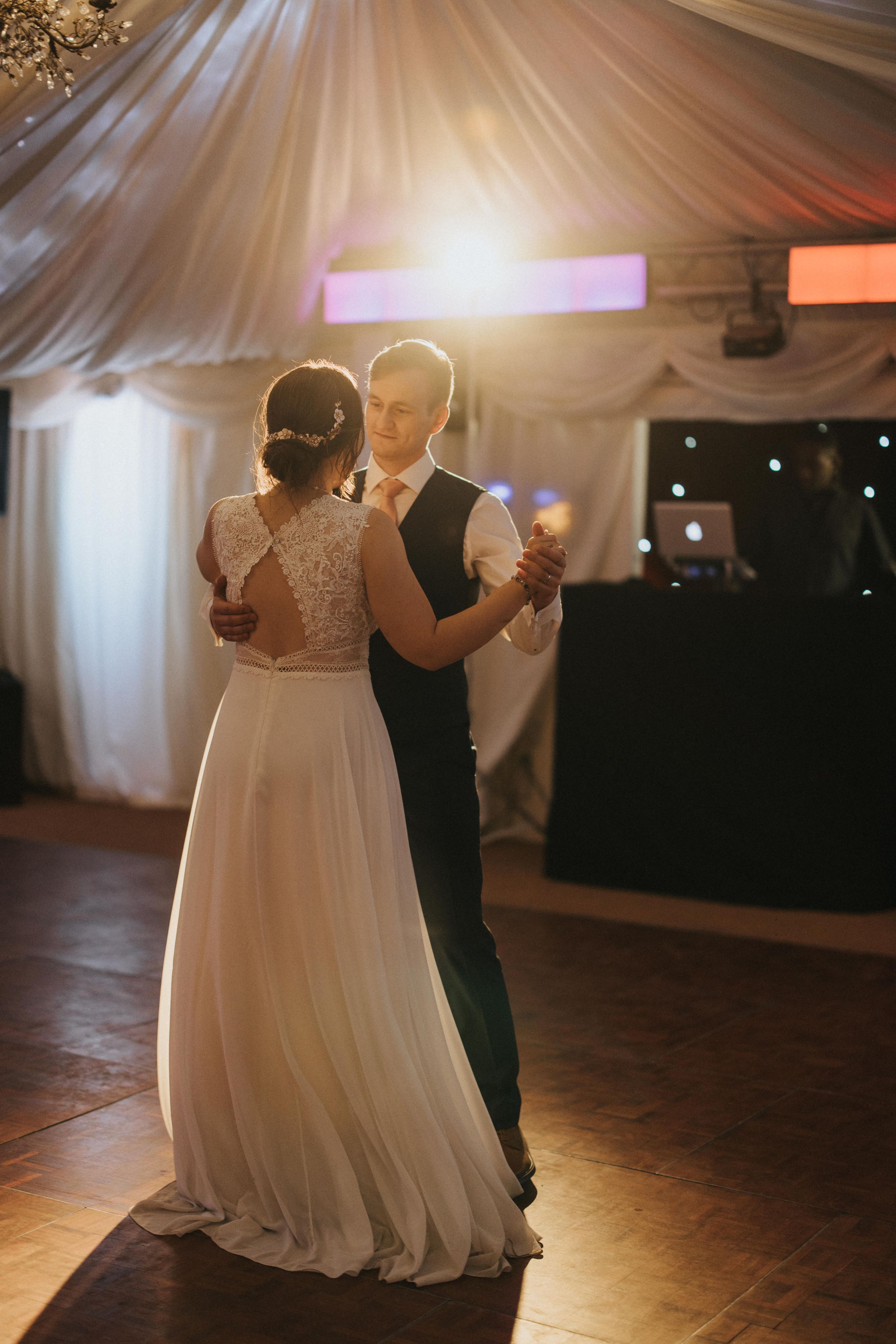 A couple shares an intimate dance at their wedding reception under soft lighting and draped decor.