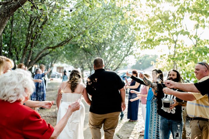Wedding guests line a pathway throwing flower petals as a couple walks through during an outdoor celebration.