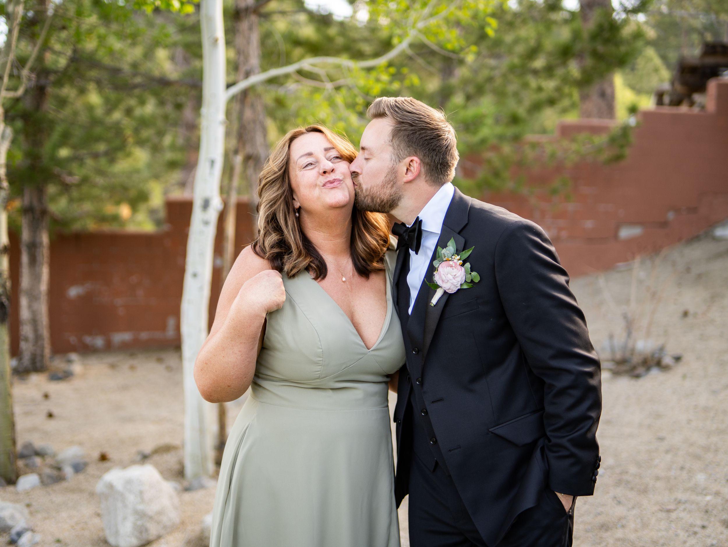 A person in a sage green dress shares a lighthearted moment with someone in a black suit outdoors.