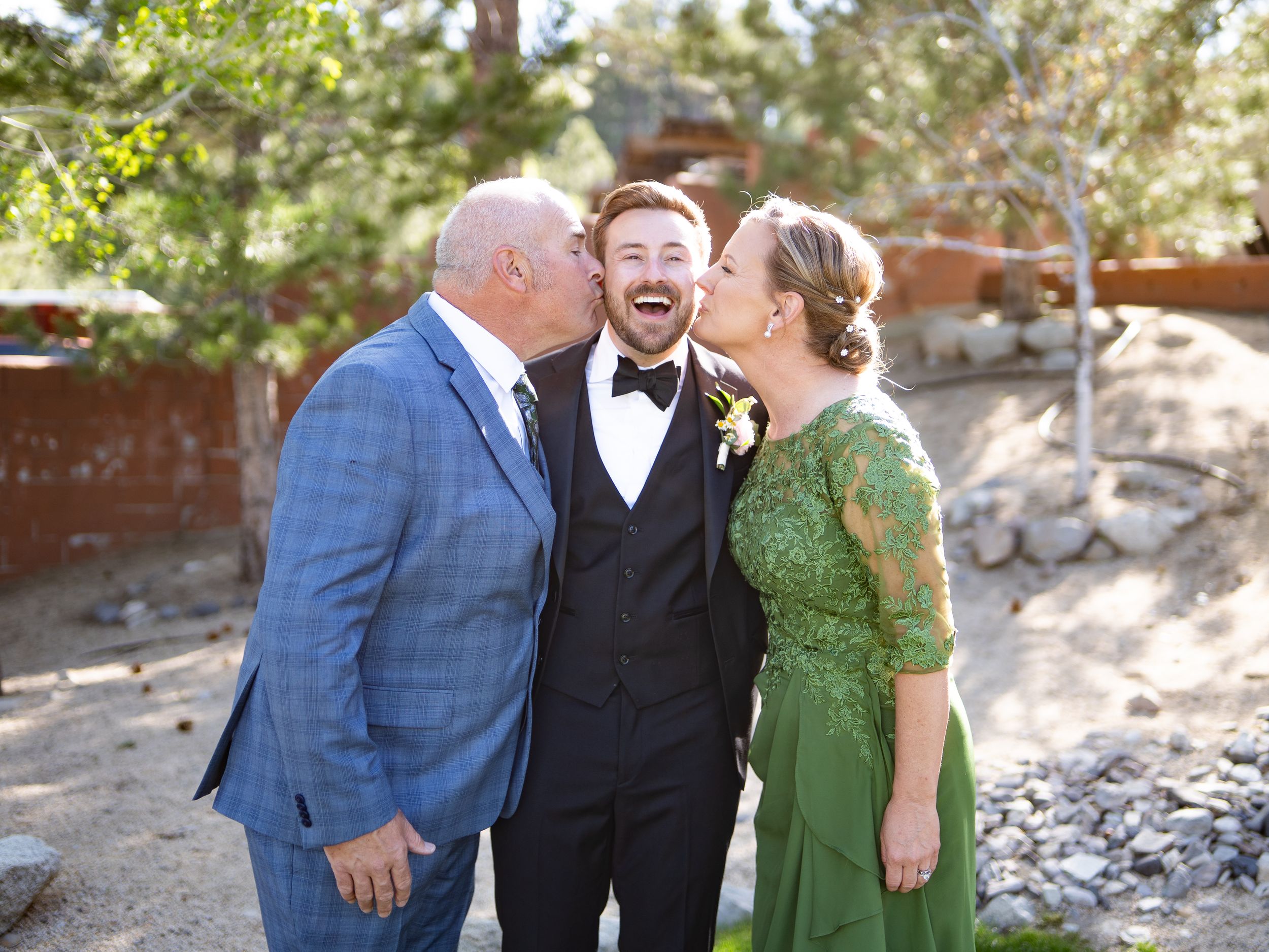 Three people in formal attire share a joyful moment outdoors as they laugh together.