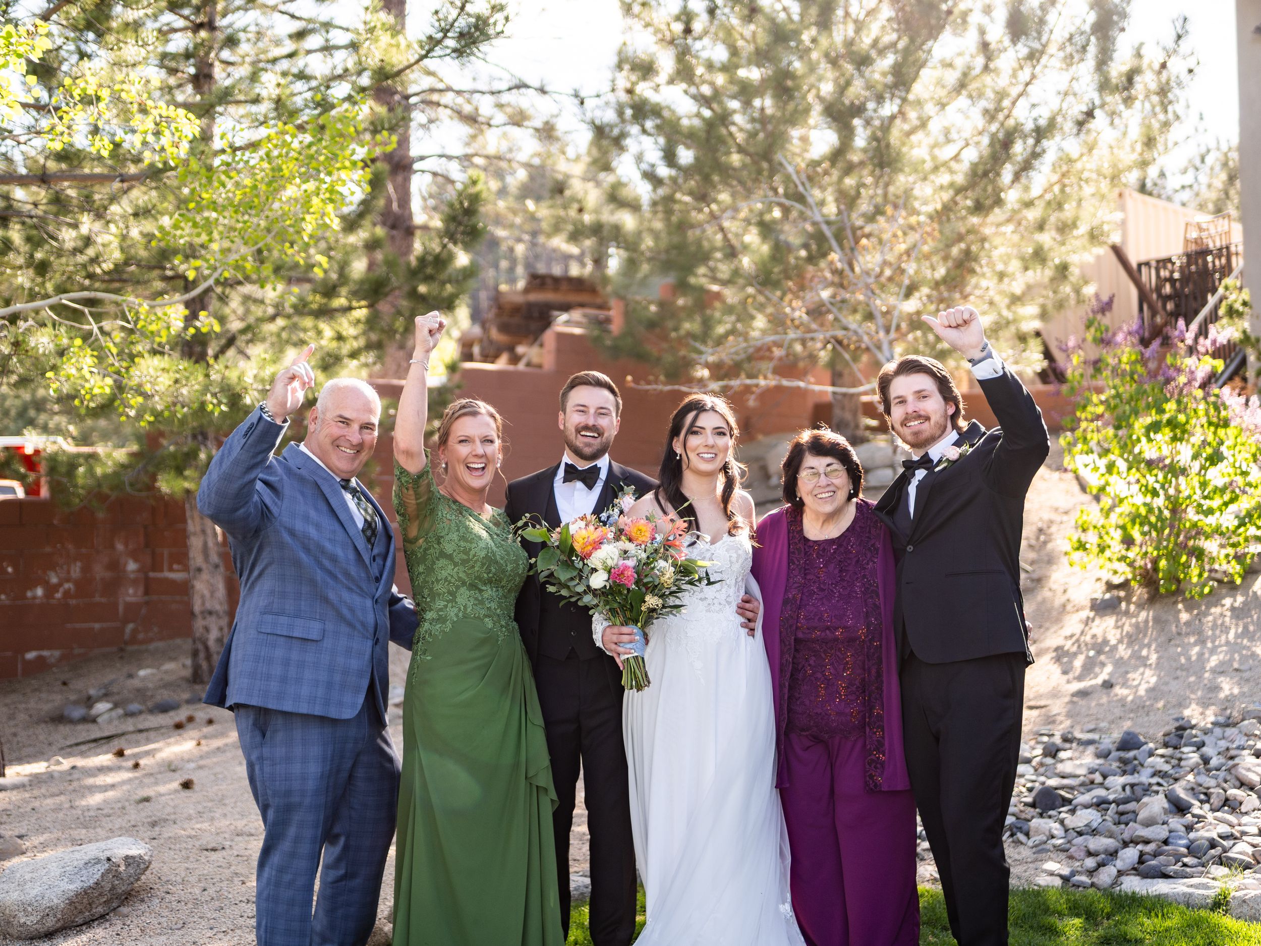 A group celebrates joyfully outdoors at a wedding ceremony surrounded by sunlit pine trees and nature.