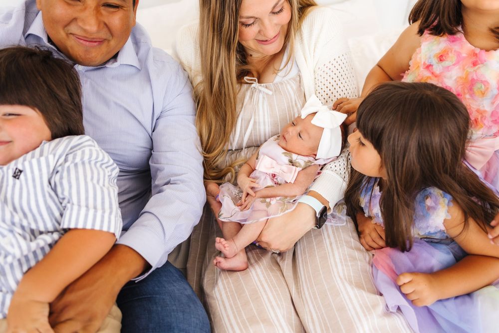 Three generations of family members sit together casually on a couch with a small baby. newborn photographer in utah newborn ph